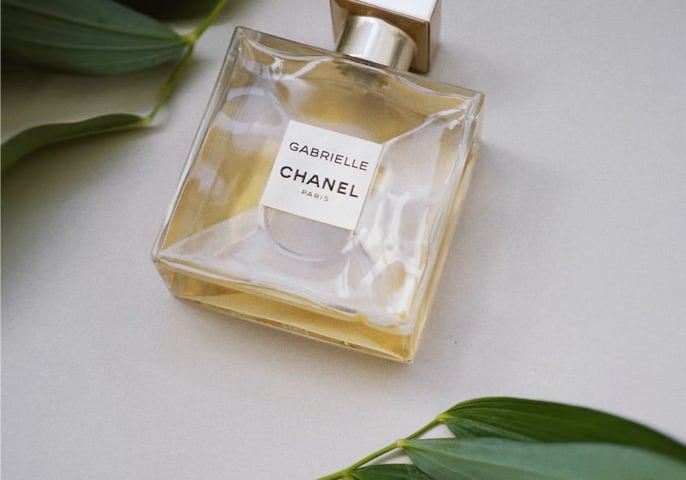 Gabrielle Essence Eau De Parfum laid down on the ground with a leaf around it.